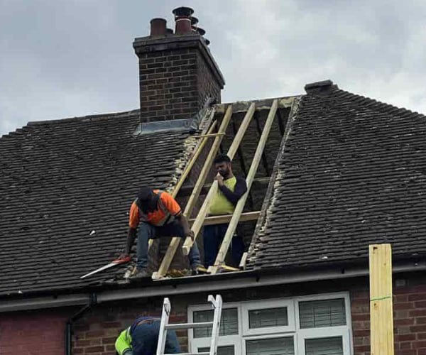 This is a photo of a roof repair being carried out. A section of the roof has been stripped and two roofers are replacing the rafters. Works being carried out by UG Roofing Hemsworth